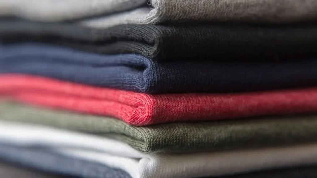 Neatly folded sweaters on a shelf showing how to make clothes last longer
